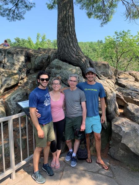 Family of four standing on a trail in front of a large tree