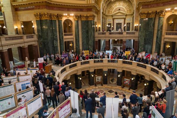 Overhead view of Madison capitol rotunda full of people and student poster presentations, speaker at a podium on left side of rotunda
