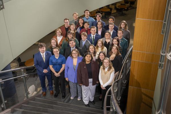 A group of students, standing in stairway, wearing business professional clothing posing for a group photo for the 67th session of Student Senate