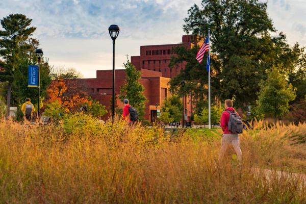 Fall on campus, student walking by tall dry grasses