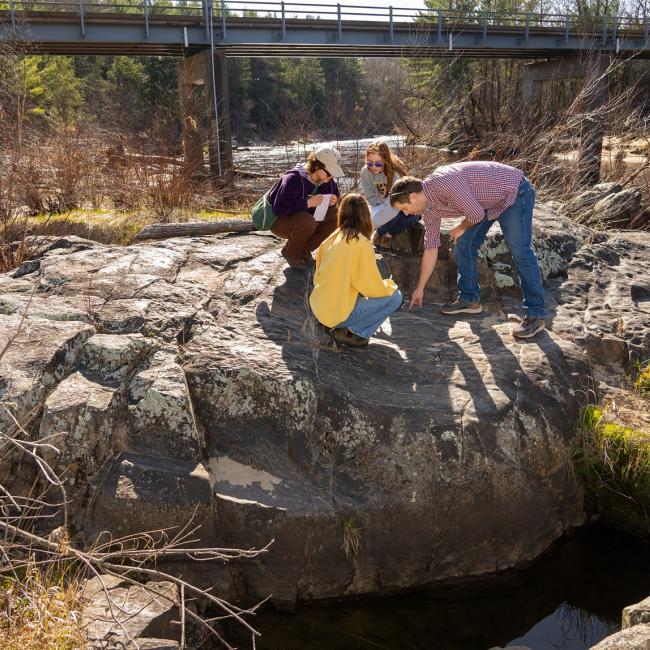 students and faculty on large river boulder for geology class 