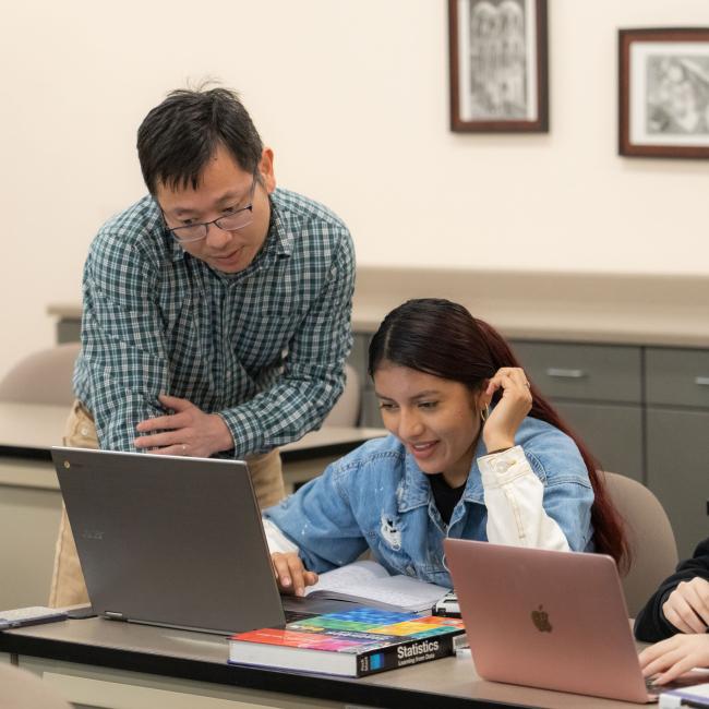 students and instructor in classroom at UWEC-BC, looking at a laptop and discussing 