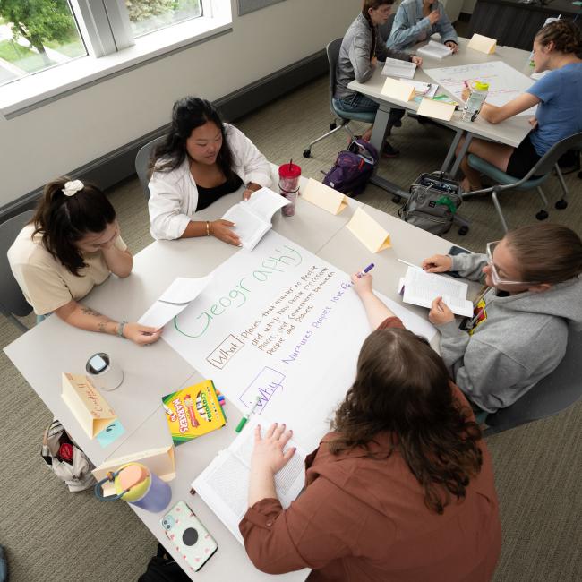 Four students at a table write on a large piece of paper during a group activity in class.
