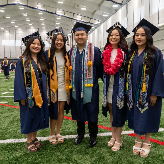 A group of graduates pose for a group photo on the football turf in the fieldhouse.