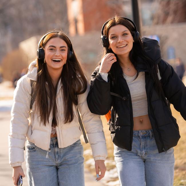 Two students walk across campus smiling at the camera.