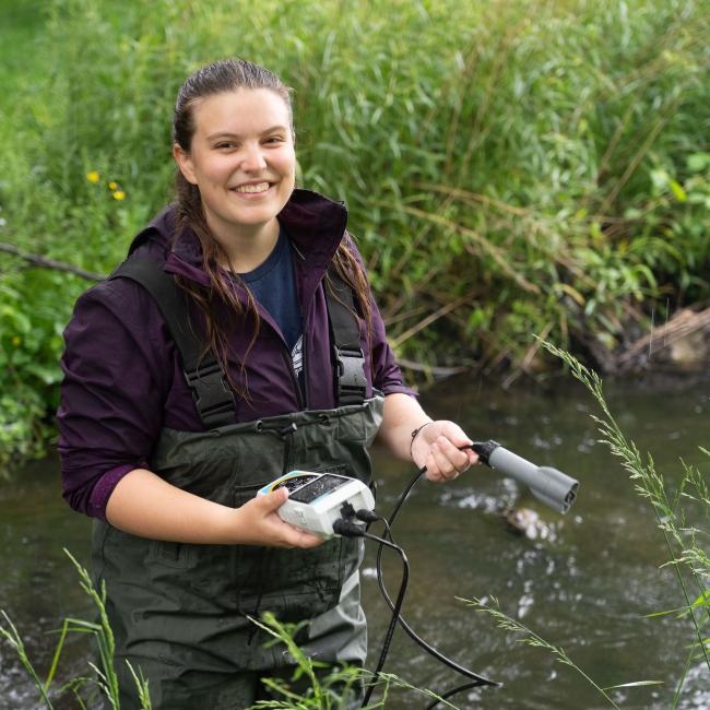 student in waders using instruments to measure creek water