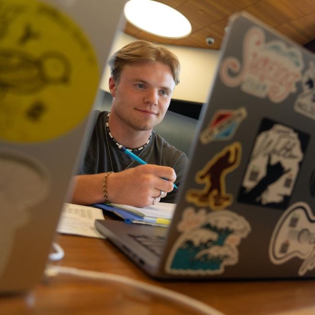 A student studies on his computer, which is covered in stickers.