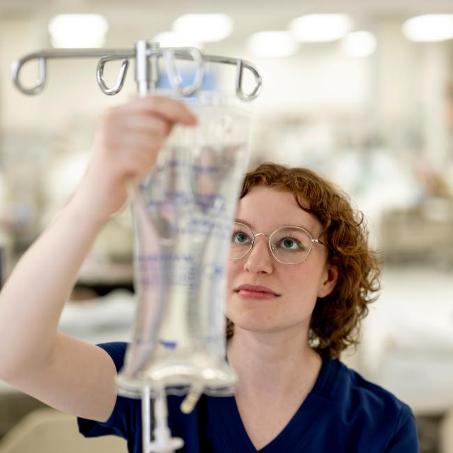 A student examines an IV bag with clear liquid in a Nursing lab.