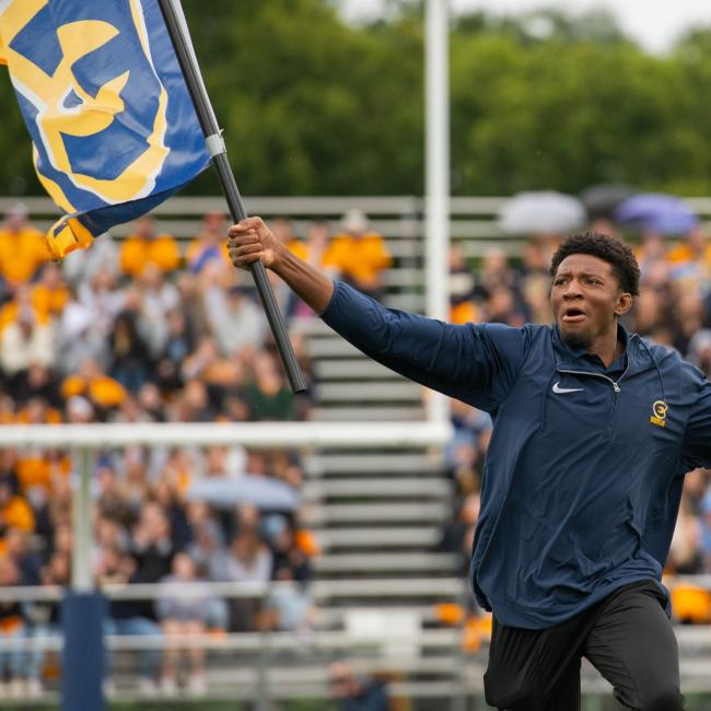 A blugold excitedly waves a UWEC flag during a football game.