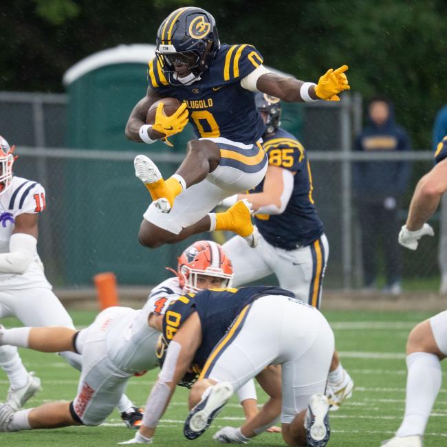 A Blugold football player hops over their opponent during the first football game of 2025.