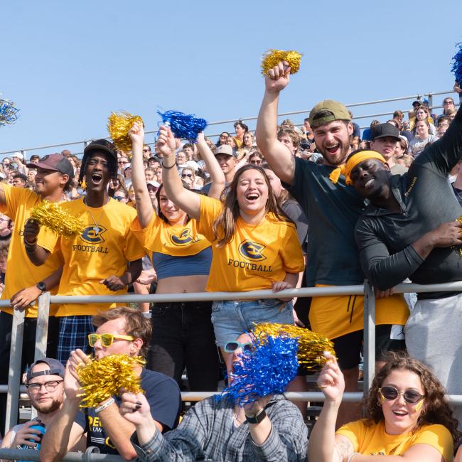 Blugolds throw their hands in the air, holding pom poms, cheering and celebrating the Homecoming football game.