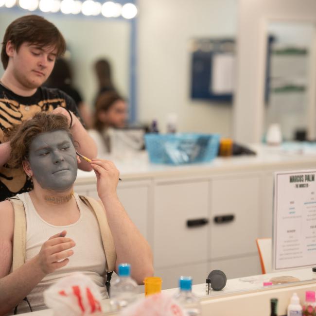 Student playing Frankenstein's monster getting makeup done before show 
