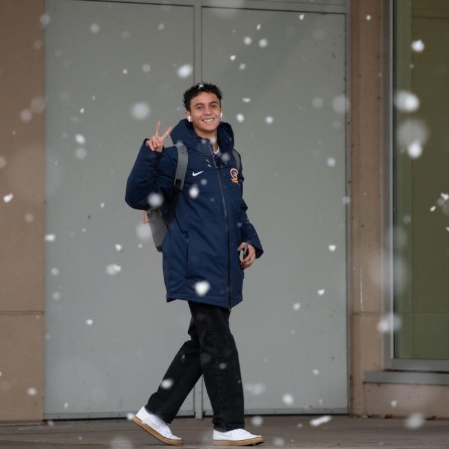 A student shows a peace sign as snow falls in the background.