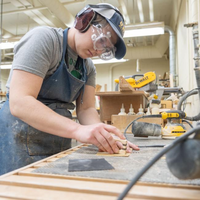 Blugold Renee Ewer concentrates while using sandpaper, surrounded by various tools.