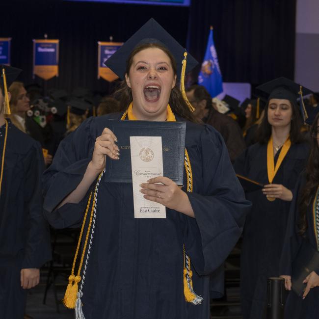 A student laughs gleefully displaying her diploma during Commencement.