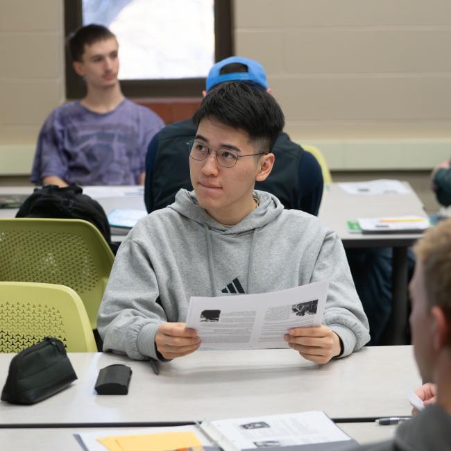 A student compares notes next to a smart board in a classroom.