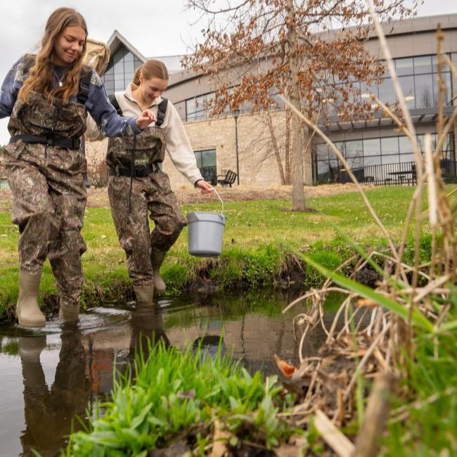 Honors students Hannah Schindler and Lexi Siegmund in camouflage waders
