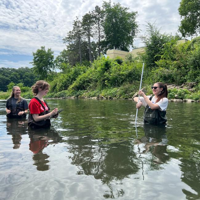 Students wade in water and smile while conducting an experiment