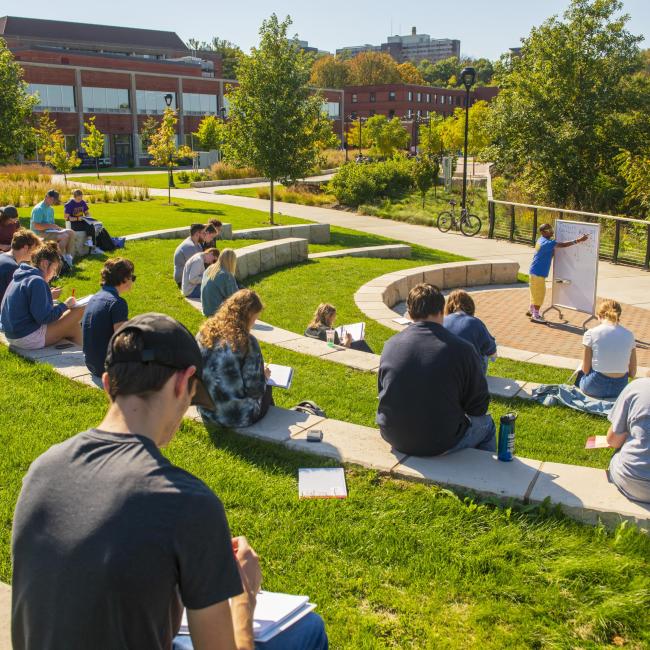 A class sits in the outdoor classroom on campus during a sunny day.