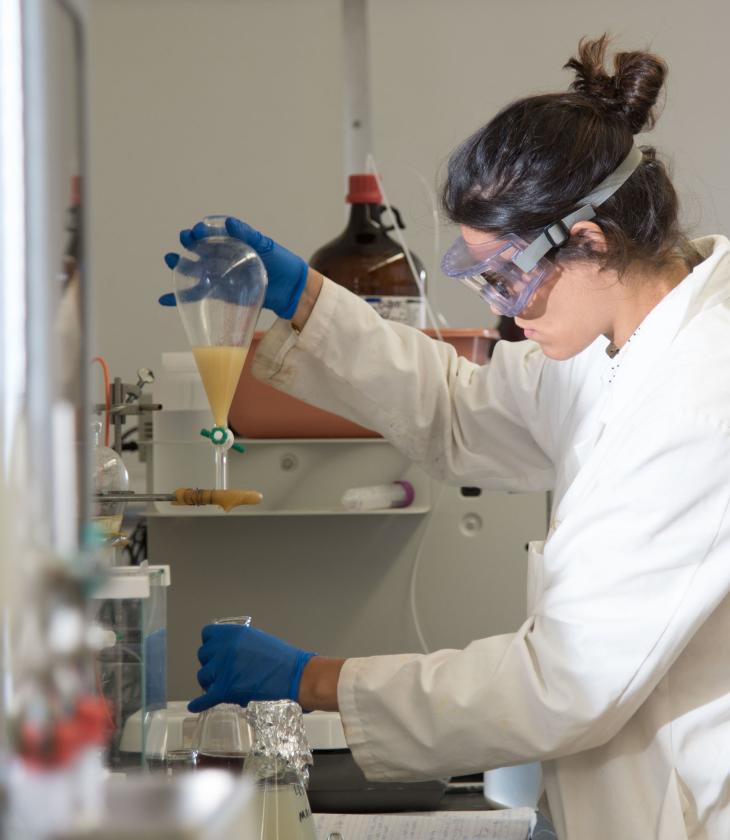 female chemistry student in lab, coat and goggles