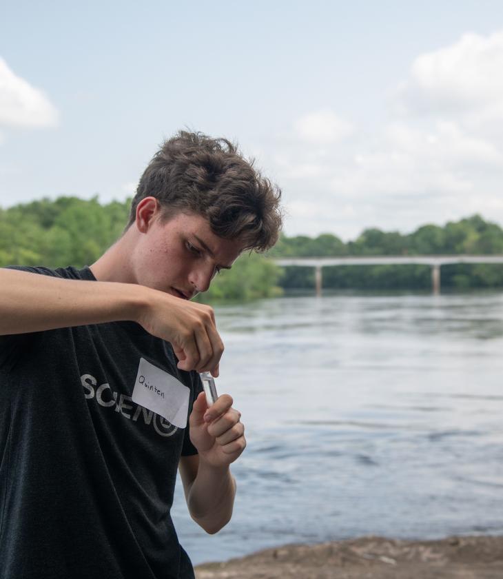 student collecting water sample at Chippewa River