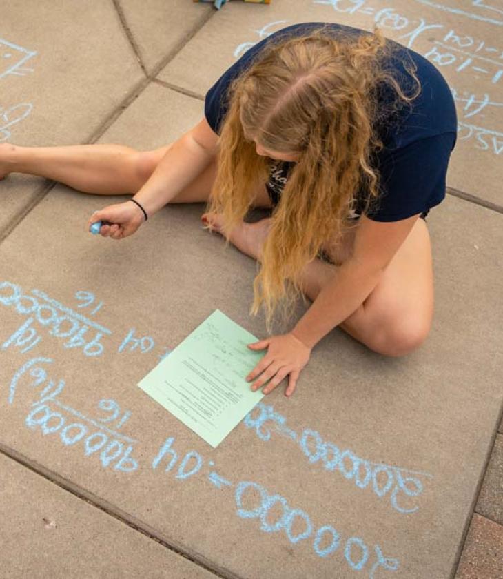 student outside doing math problem on sidewalk for class 