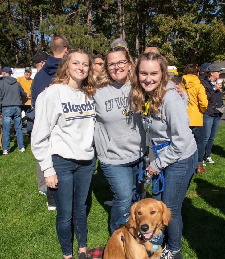 Three alumni in Blugold sweatshirts with a dog.