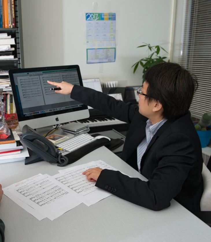 Two people look at a computer screen showing sheet music