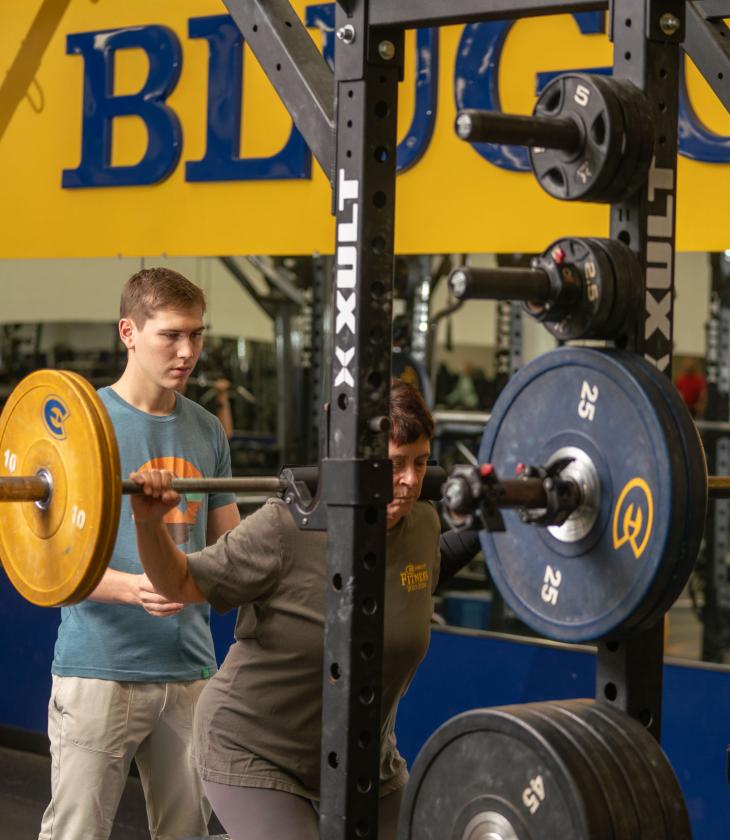 student spotting a client doing a squat in the weight room