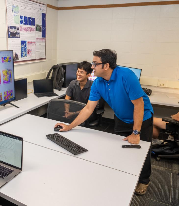 A professor and a student smile while working on a large computer together.