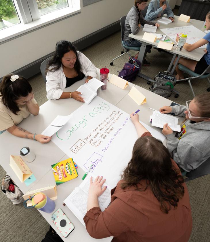 Four students at a table write on a large piece of paper during a group activity in class.
