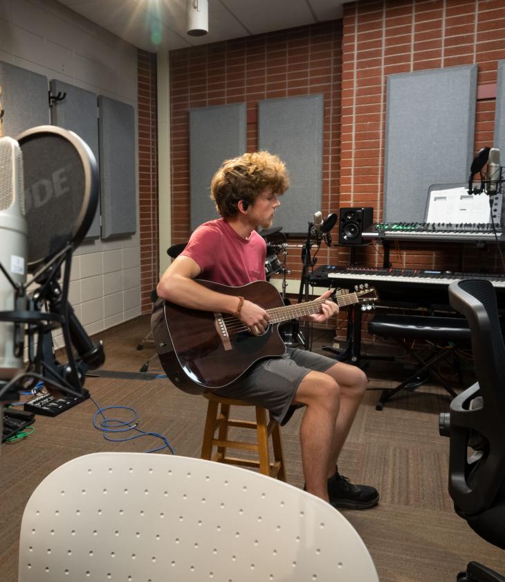 Student plays the guitar in UWEC's audio room