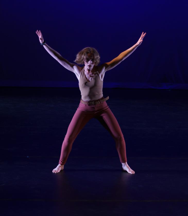 Dancer barefoot on stage extends arms and legs into an "x" formation