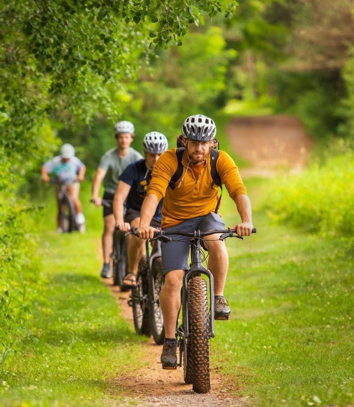 A group of bikers ride through a grassy trail in the summer