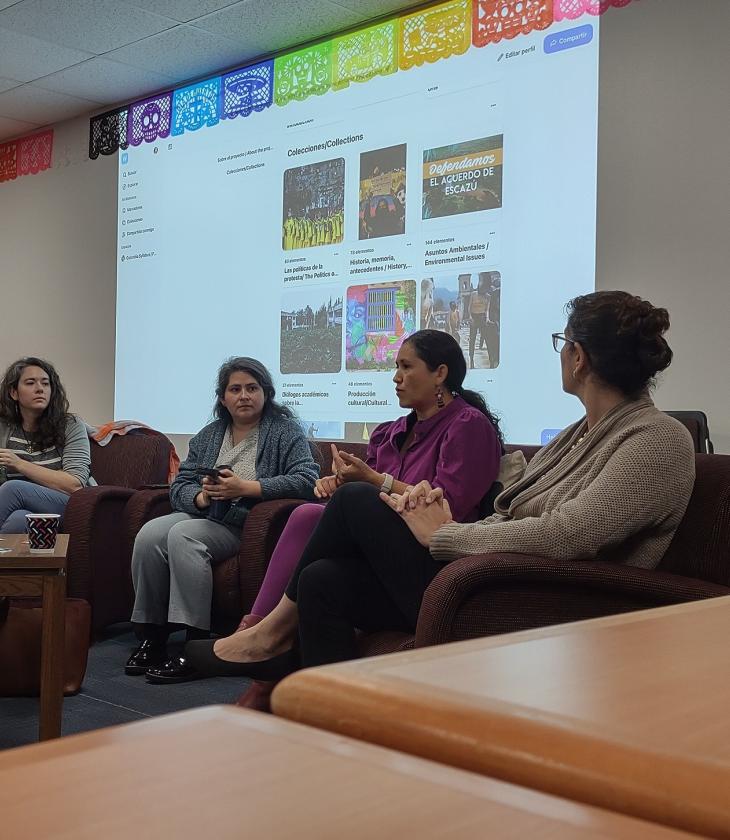 A panel of speakers sit in front of a projector screen at an event.