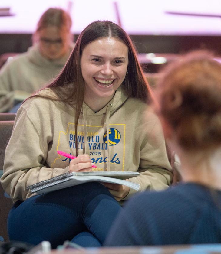 A student smiles brightly while taking notes.