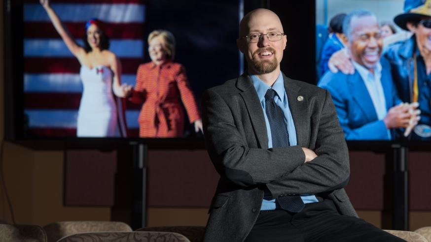 Eric Kasper with tv ads for elections behind him 