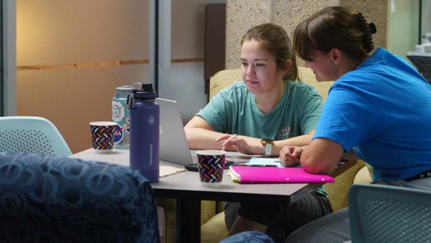 two female students talking and looking at a laptop at a small table