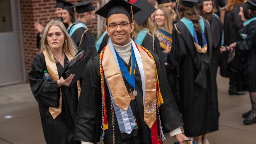 graduate in cap and gown with many honors cords and stoles