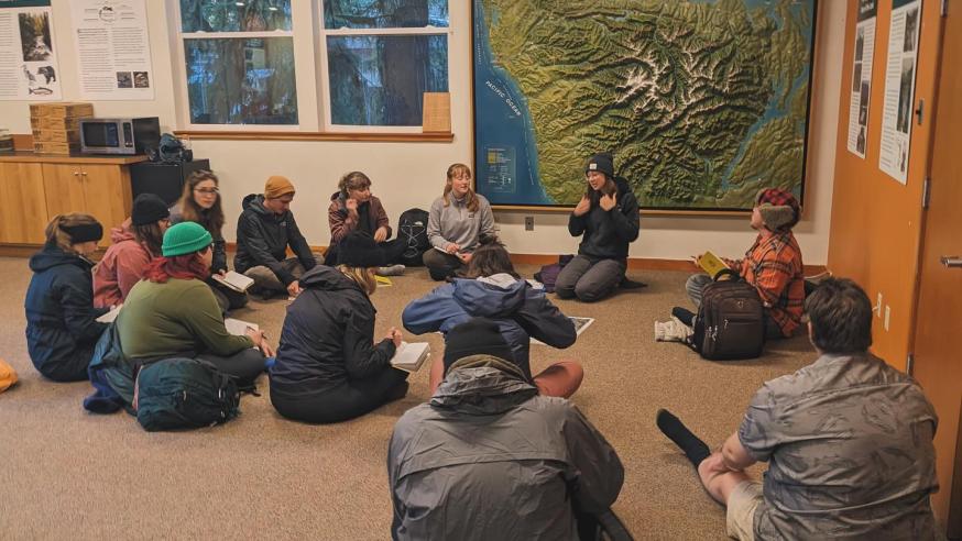 students seated on the floor in a national park center listening to guide