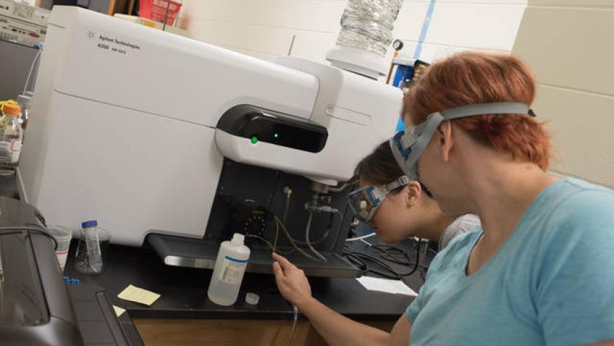 Two students wearing googles use a piece of chemistry lab equipment