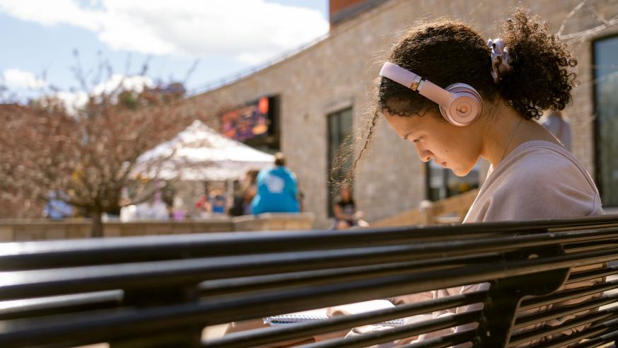 female student on a bench listening to music on headphones 