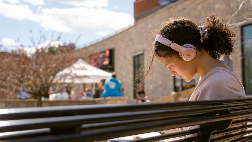 female student on a bench listening to music on headphones