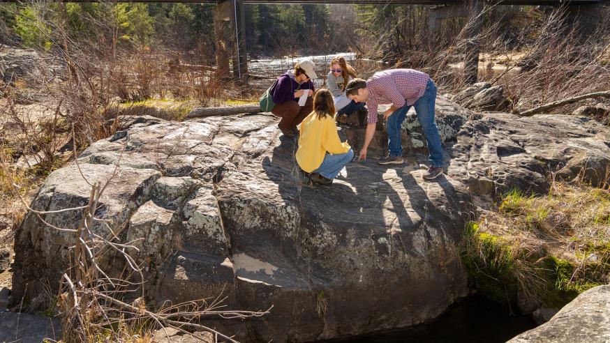 students and faculty on large river boulder for geology class