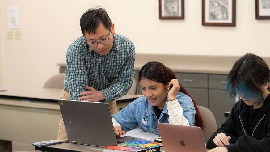 students and instructor in classroom at UWEC-BC, looking at a laptop and discussing