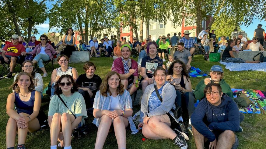A large group of students smiles for the camera while sitting on a grassy hill.