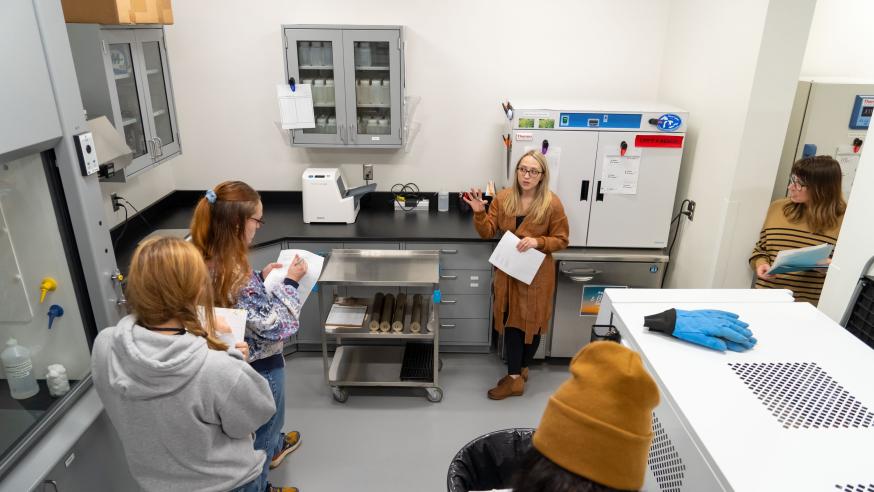 Students take notes while listening to someone talk to them in a lab setting
