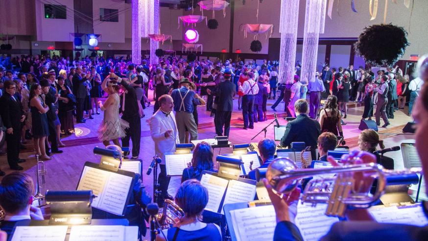 A large ballroom with a music performance and couples dancing wearing 1920's outfits