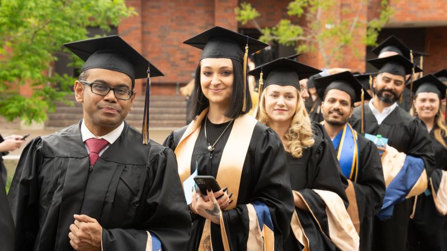 Students wearing black graduation caps and gowns walk in a line and smile for a photo.