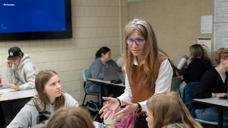 A faculty member speaking with a table of students inside a classroom.